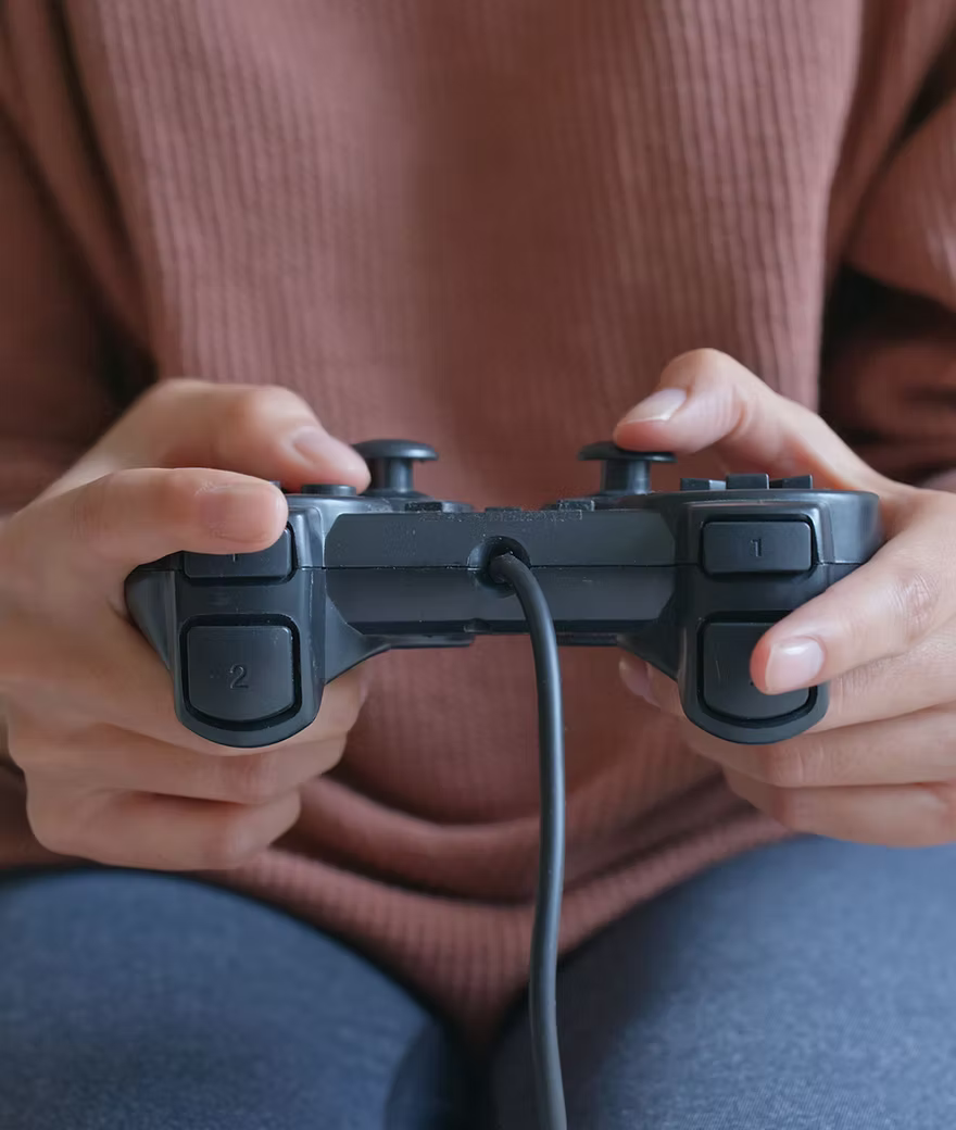 Une manette de jeu tenu dans les mains de quelqu'un qui joue.